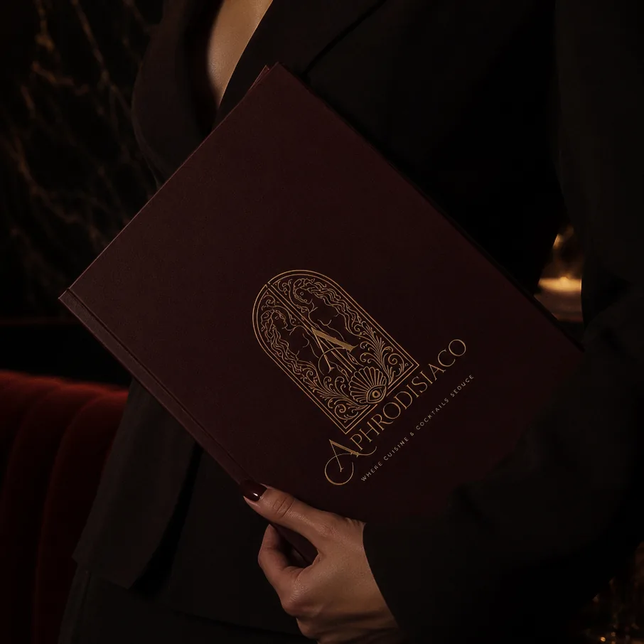 Burgundy Aphrodisiaco cocktail menu with gold logo held by a guest